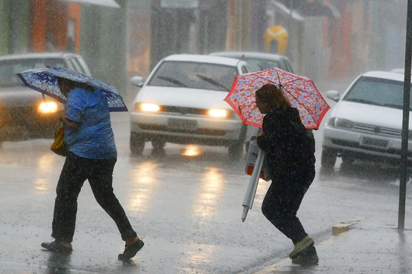 Pedestres correm da chuva tentando atravessar rua em frente a Santa Casa de Franca